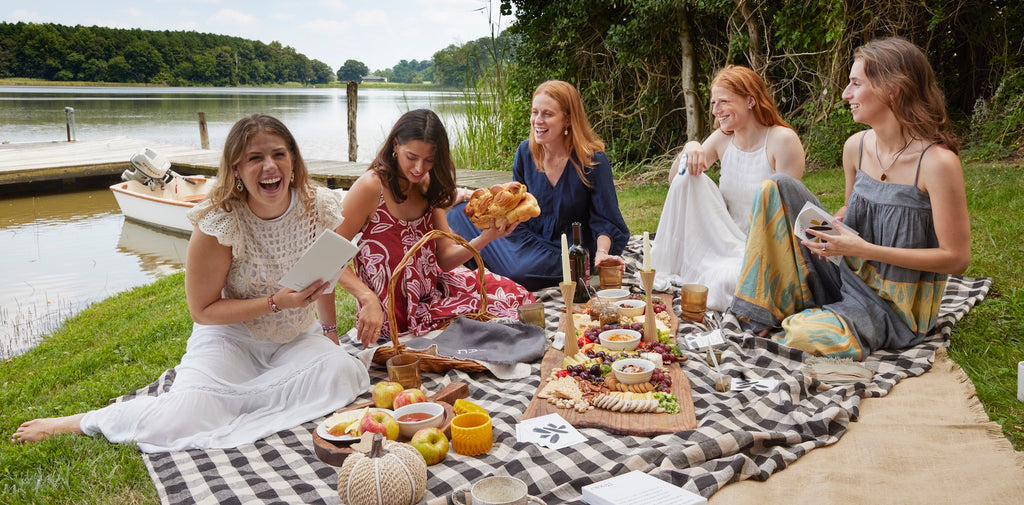 Group of 5 women gather around picnic to celebrate Shabbat with fall festive colors and foods