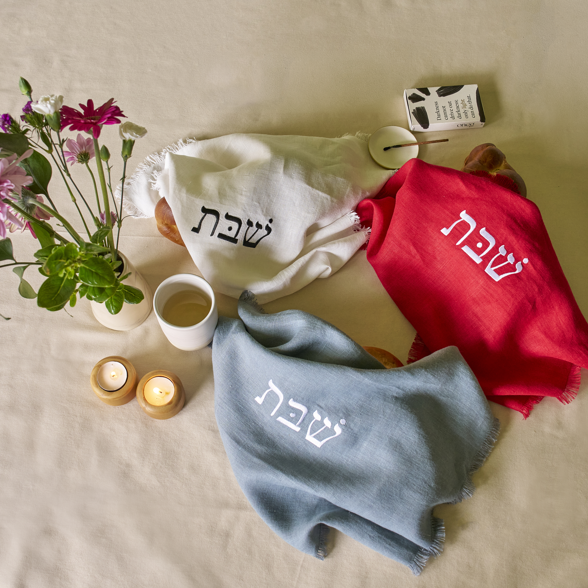 set of three embroidered linen challah covers in red, white, and blue on a shabbat table